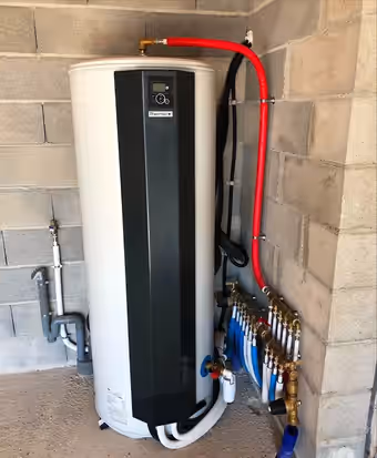 Chauffe-eau thermodynamique noir posé contre un mur de parpaings, raccordé à un collecteur